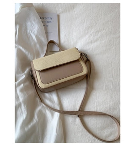 Detail of khaki leather crossbody bag with woven texture and top handle on white fabric