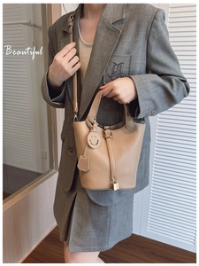 Detail of beige lychee textured bucket bag with side lock and leather smiley charm