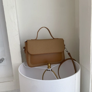 Brown leather and woven crossbody bag with top handle shown from a 45-degree angle