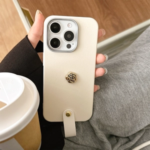 Detailaufnahme einer cremeweißen Leder-iPhone-Hülle mit goldener Kamelie und Handgelenkschlaufe