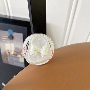 Detailed macro of a cream bow phone grip featuring Good Luck text and pearl texture