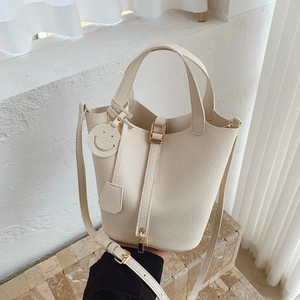 Chic cream leather bucket bag with top handles and a smile charm in a minimalist setting