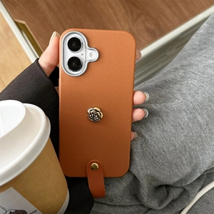 Nahaufnahme der orangen Leder-iPhone-Hülle mit goldener Kamelie und Handgelenkschlaufe