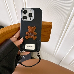 Detail of plush brown teddy bear and Goodluck label on black leather iPhone case with lanyard
