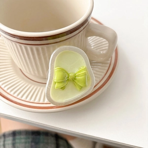 Detail of light green 3D bow phone grip with glossy resin finish next to a cup