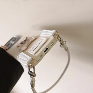 Detail of cream iPhone case showing plush decor, wrist strap, and metal carabiner clips
