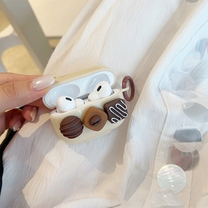 Detail of a cream AirPods Pro case featuring three 3D chocolate designs and a hook.