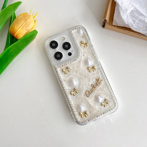 Détail de la coque iPhone avec nœud, perles et strass à côté de tulipes jaunes
