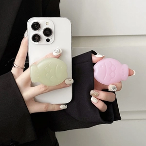 Detail showing pink and green fish-shaped phone pop sockets held on white iPhone