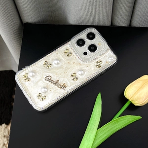 Détail de la coque iPhone nacrée avec nœud doré, perles et bordure en strass