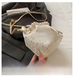 Detail of embroidered floral bucket bag with large pearl handle and woven metal chain strap
