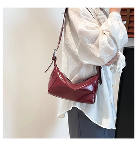 Detail of adjustable metal buckle and shiny burgundy patent leather on underarm bag
