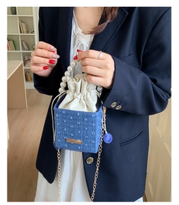Dettaglio borsa a secchiello in denim blu con manico di perle e catena dorata