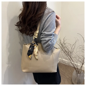 Detailed shot of beige leather tote bag featuring a decorative printed scarf on the handle