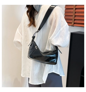 Side view of black glossy patent leather shoulder bag with wide strap and silver hardware