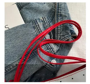 Detail shot of the red leather handle and black heart print on white shoulder bag