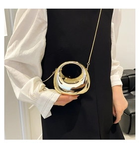 Detail of a hollow circular gold mirror-finish metal handbag with a sleek chain strap