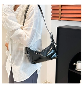Close-up of a black glossy underarm bag with silver zipper detail and adjustable strap