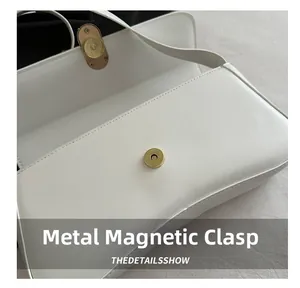 Détail du fermoir magnétique doré sur un sac bandoulière en cuir blanc avec coutures
