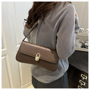 Detail of dark brown leather shoulder bag with a gold metal buckle worn by a model