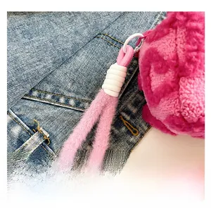 Detalle de bolso de peluche rosa con asa de nudo suave y eslabón circular blanco
