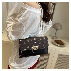 Detail of cherry-patterned shoulder bag with gold chain strap worn by a model