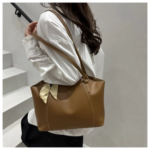 Detail of a brown leather tote bag with white contrast stitching and a printed silk scarf