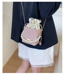 Borsa a secchiello rosa con coulisse, manico di perle e catena d'oro indossata da modella