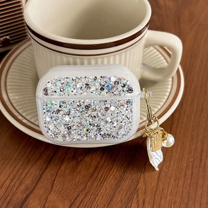 Detail of silver glitter AirPods Pro case with gold hook and pearl on a wooden table