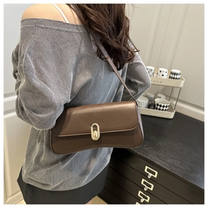 Detail of a brown leather shoulder bag with gold clasp shown on a model's arm