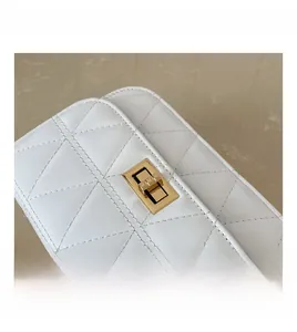 Detail of a gold rectangular swivel lock on a white quilted leather bag with chain
