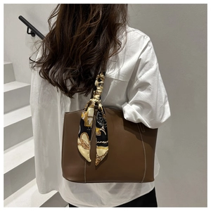 Brown faux leather tote bag with printed silk scarf on handle, shown on a model