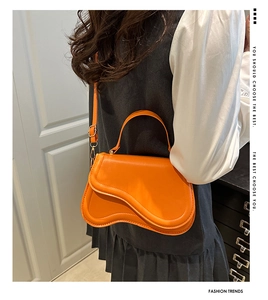 Detailed view of the bright orange leather saddle bag with unique curved flap and slim strap