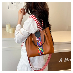 Detail of a brown leather tote with colorful ethnic woven strap and dual carry handles