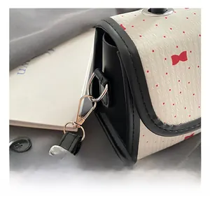 Detail of silver metal hook and black strap on a white pink bow pattern shoulder bag
