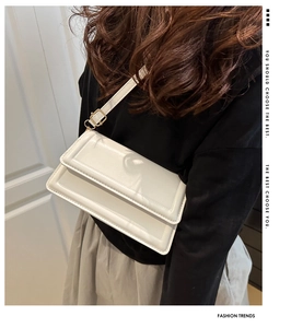 Detail of white glossy shoulder bag with adjustable gold buckle and sleek flap design