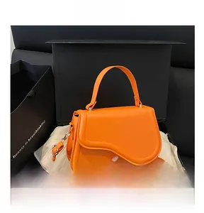 Detail of a bright orange crossbody bag with a wavy flap in a black gift box