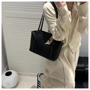 Detail of black leather tote bag with white stitching and decorative silk scarf on handle