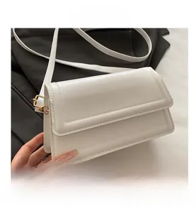 Detail shot of white rectangle flap crossbody bag with thin strap and gold metal hardware