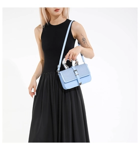 Detail of light blue crossbody bag featuring woven texture and silver metal ring handle
