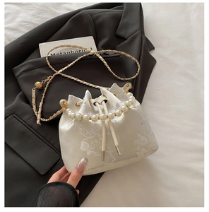 Detail of floral embroidery and pearl handle on a beige drawstring bucket bag