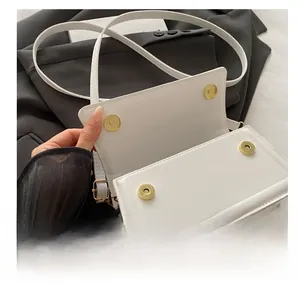 Detail view of white crossbody bag with dual golden magnetic snaps on black blazer