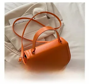 Detail of orange minimalist crossbody bag featuring gold metal hardware and top handle