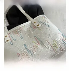 Close-up of white tote bag featuring colorful wave embroidery and gold rivet hardware