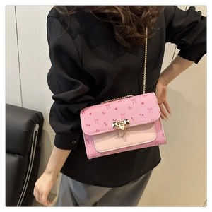 Close-up of pink cherry crossbody bag with bow patterns and golden lock on model