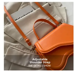Detail view of adjustable strap buckle on vibrant orange saddle bag with pebble texture