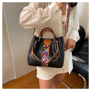 Close-up of black leather tote bag with colorful geometric woven straps and wood handles