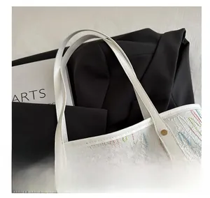 Close-up of white tote bag featuring colorful wavy embroidery and gold rivet details