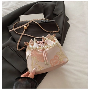 Detail of pink embroidered bucket bag featuring pearl handle and golden heart chain strap