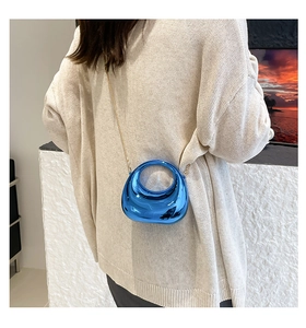 Blue metallic crescent evening bag with gold chain worn over a beige sweater